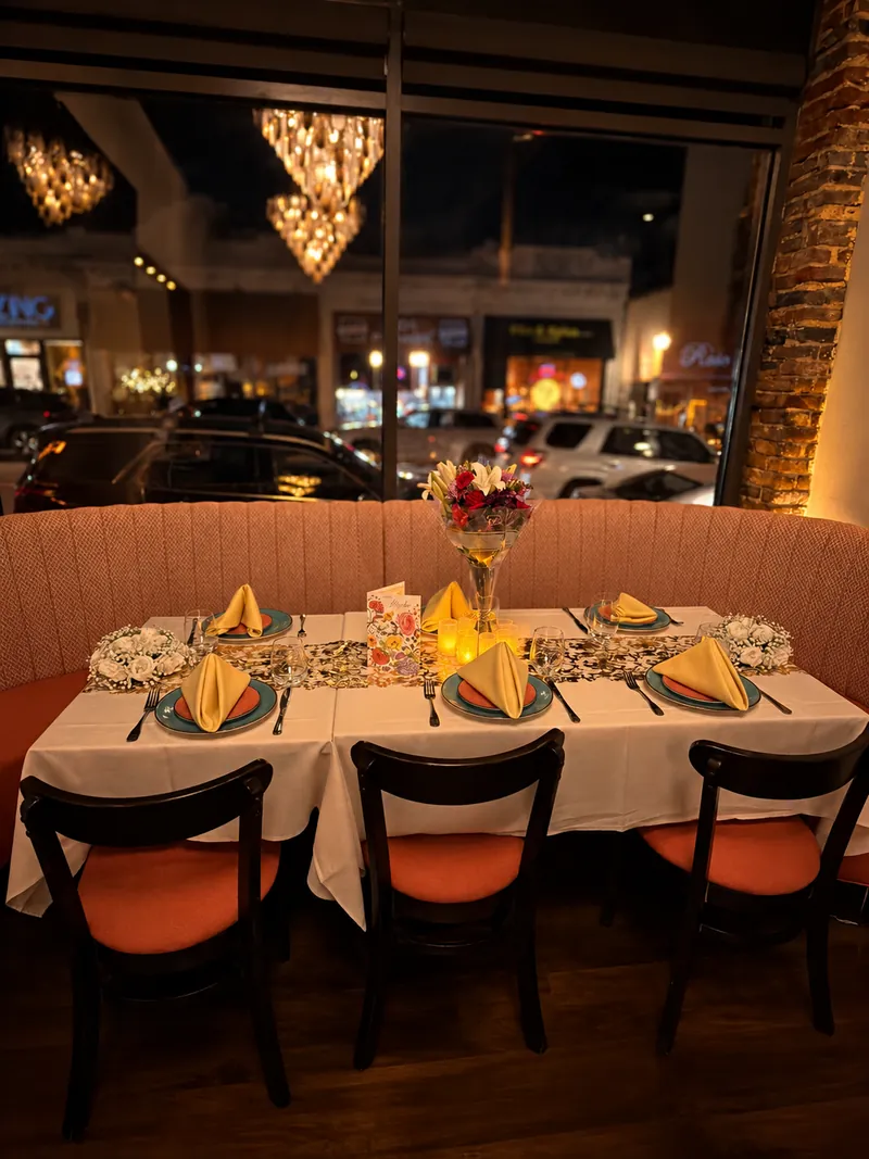 A window booth at Rassa on Moody Street set with fresh flowers, candles, a greeting card and a golden table runner